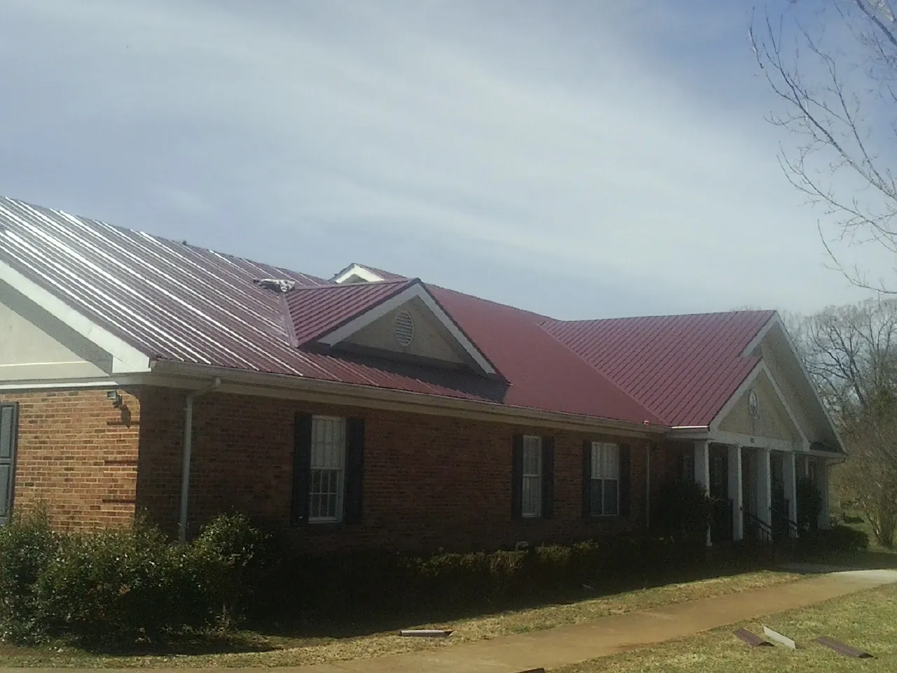Red metal roof with gabled entries on a long brick building, from a Hail Damage Roof Repair job in Lovejoy