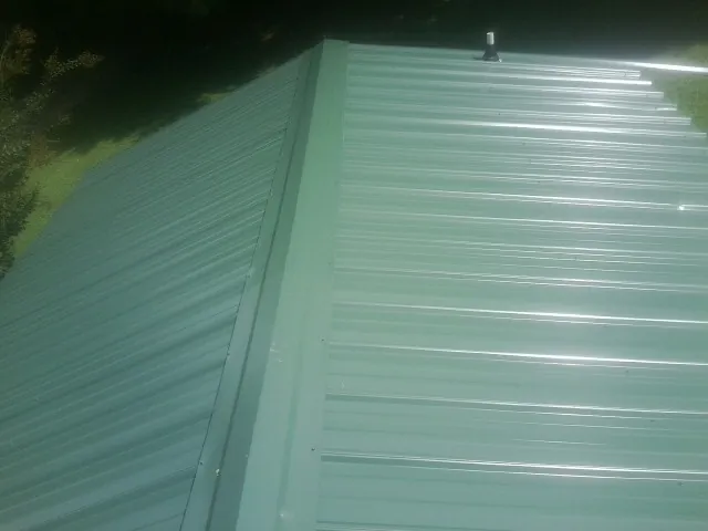 New green metal panels meeting at the ridge of a roof — Flat Roof Repair work by our crew in Lovejoy